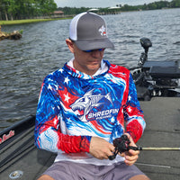 Man wearing a ShredFin patriotic red, white, and blue hooded performance fishing shirt with UPF 50+ sun protection on a fishing boat.