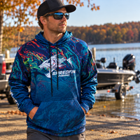 Man wearing a ShredFin StormSurge Electric Swirl Elite Performance fishing hoodie by a lake and bass boat.