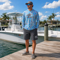 A man wearing a colorful retro camo ShredFin Fishing UPF 50 hooded performance shirt and gray HookSet fishing shorts.