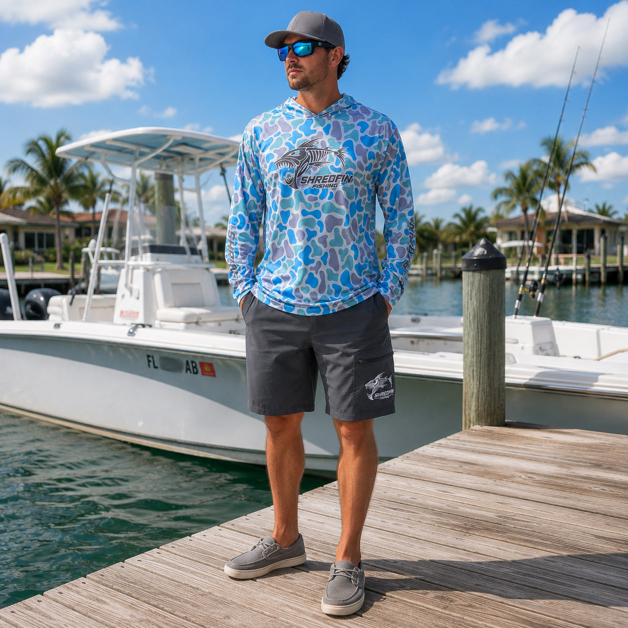 A man wearing a colorful retro camo ShredFin Fishing UPF 50 hooded performance shirt and gray HookSet fishing shorts.
