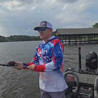 Video of a man on boat wearing a ShredFin patriotic red, white, and blue hooded performance fishing shirt, showing the fit and design from multiple angles.