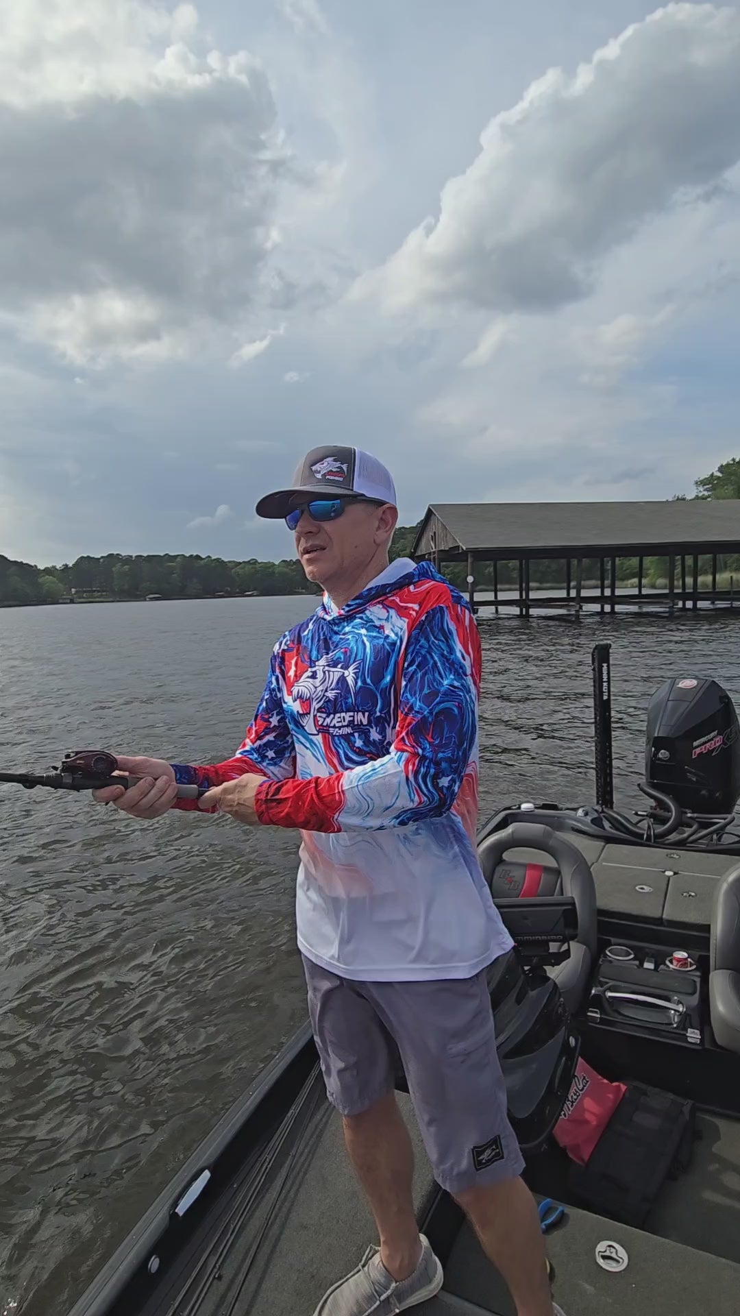 Video of a man on boat wearing a ShredFin patriotic red, white, and blue hooded performance fishing shirt, showing the fit and design from multiple angles.